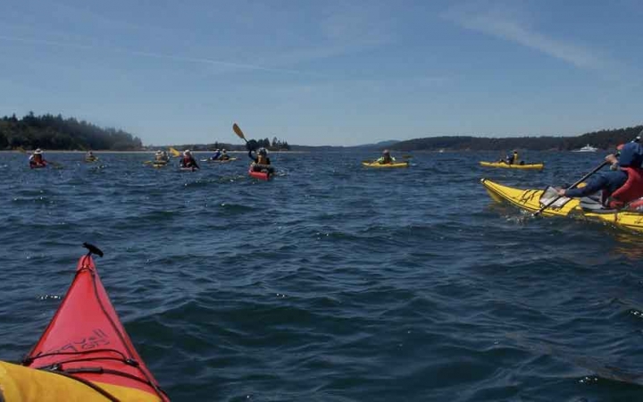 a group of kayakers paddle a large blue lake on a gap year expedition with outward bound